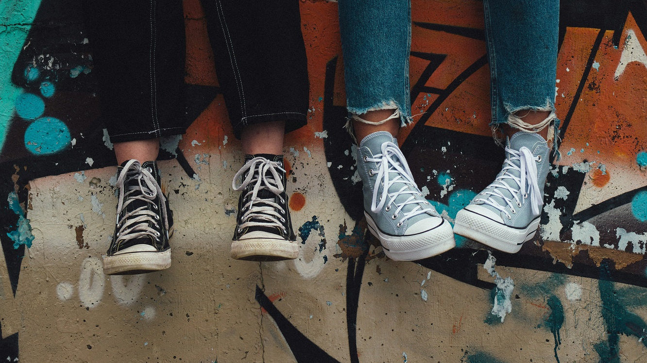 SURPRISA Blog Teenager und Geldgeschenke zwei Jugendliche sitzen auf einer Mauer man sieht nur ihre Beine und Füße blauen Jeans in schwarz-weißer Converse All Star High Top Sneakers