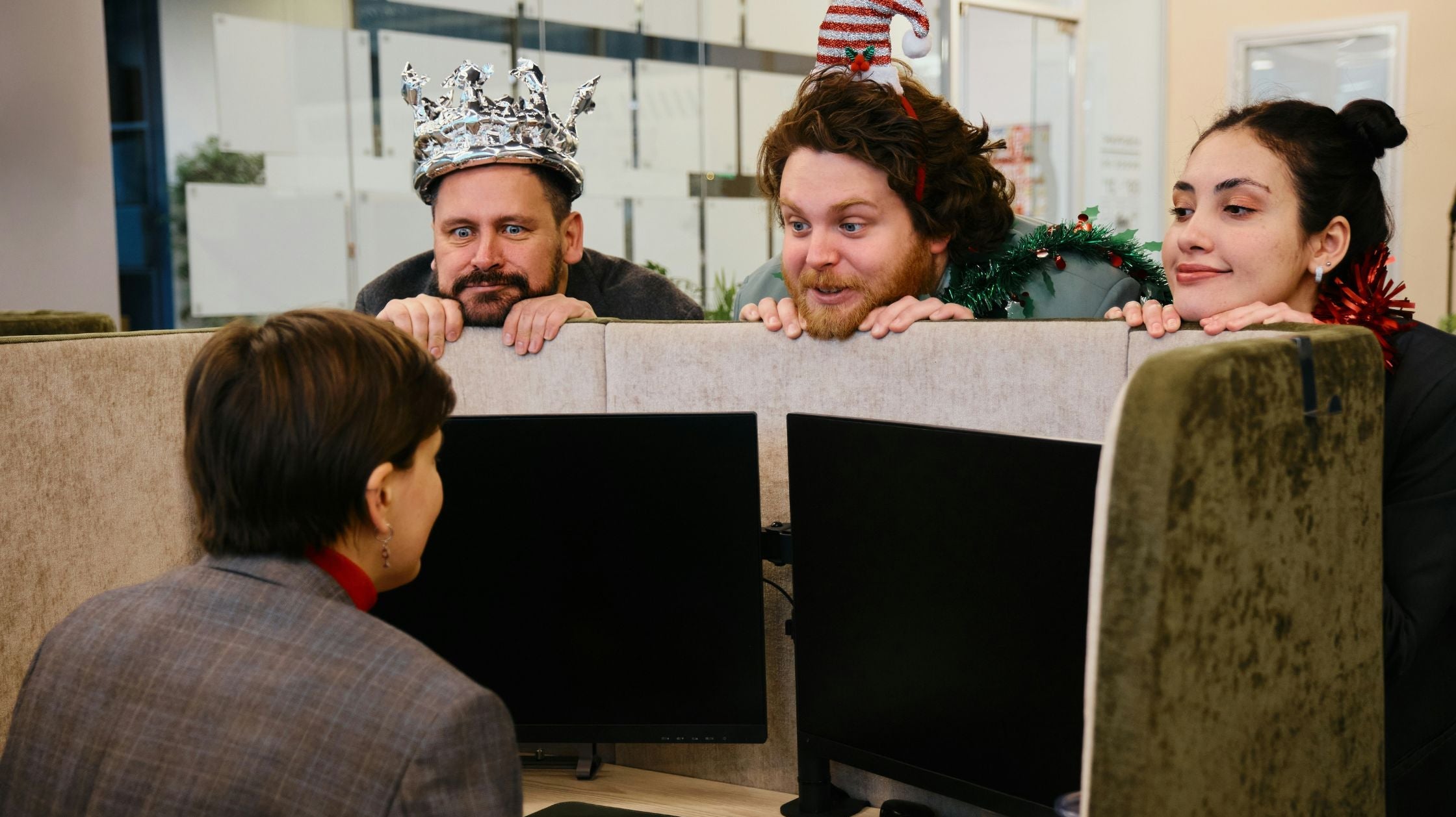 Kollegen mit Weihnachtsdeko schauen lachend über Büroabtrennung – kreative Geschenkideen fürs Büro-Wichteln