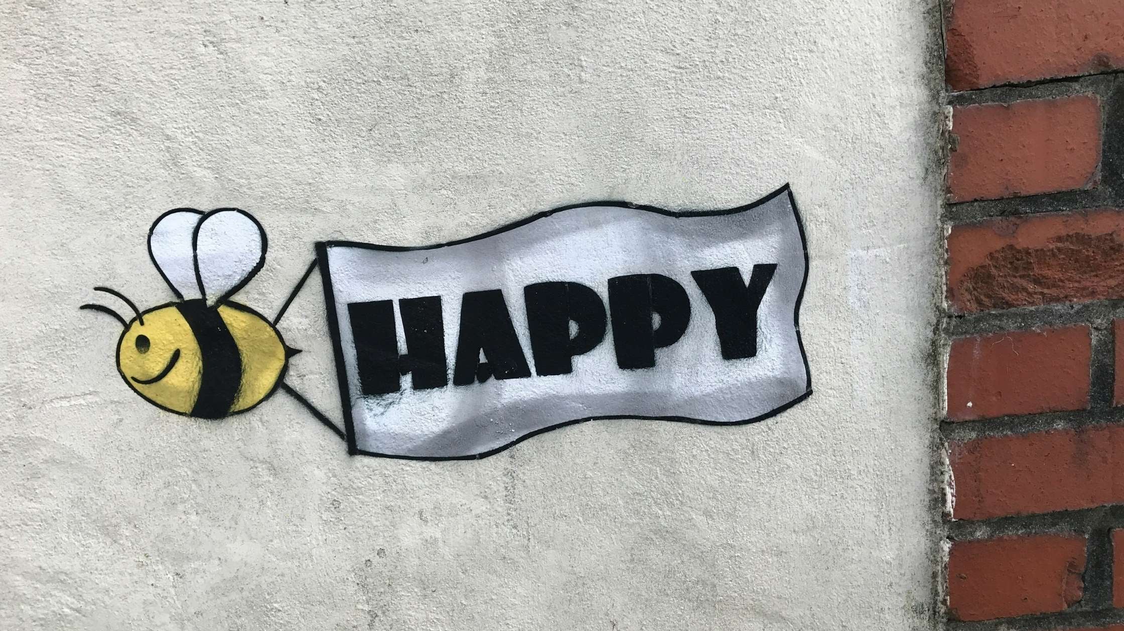 Graffiti einer lachenden Biene mit HAPPY-Banner an Hauswand – fröhliche Idee für kleine Geschenke mit großer Wirkung