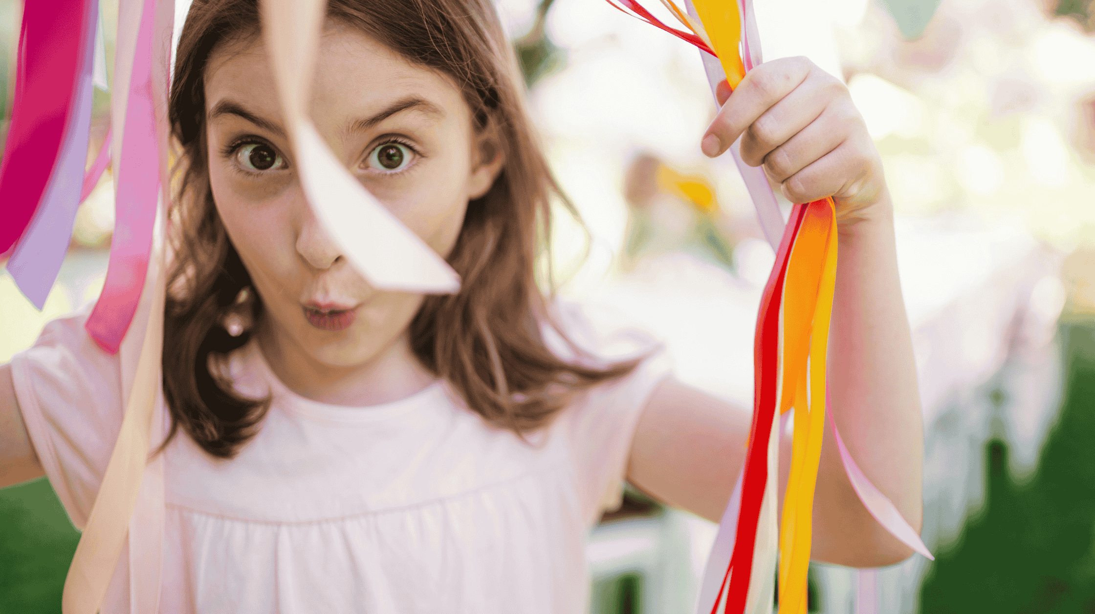 Mädchen blickt lächelnd durch bunte Bänder – Symbol für die kindliche Freude am Schenken