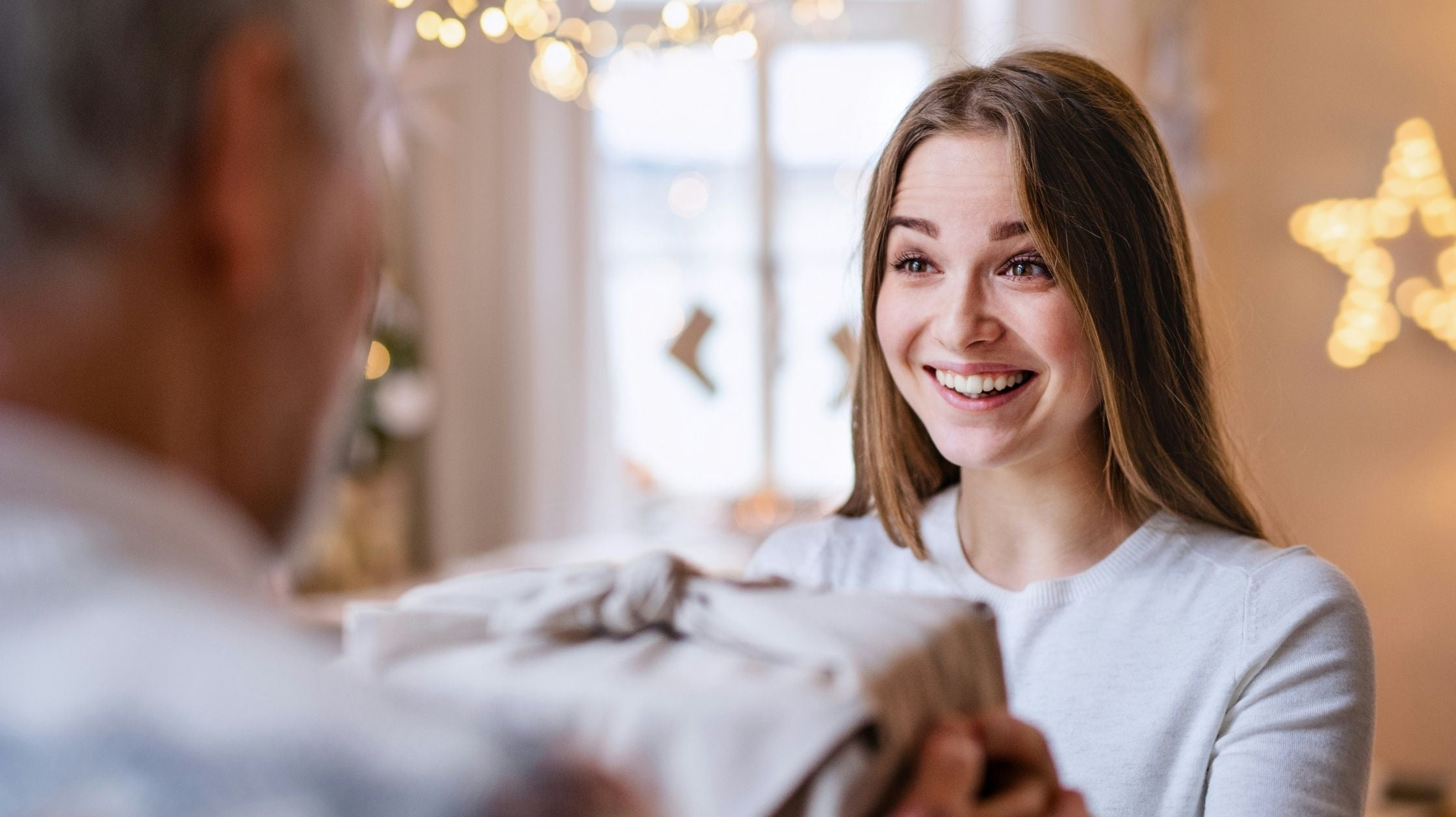 Junge Frau freut sich überrascht über ein Geschenk – stimmungsvolle Weihnachtsideen für Teenager und junge Erwachsene