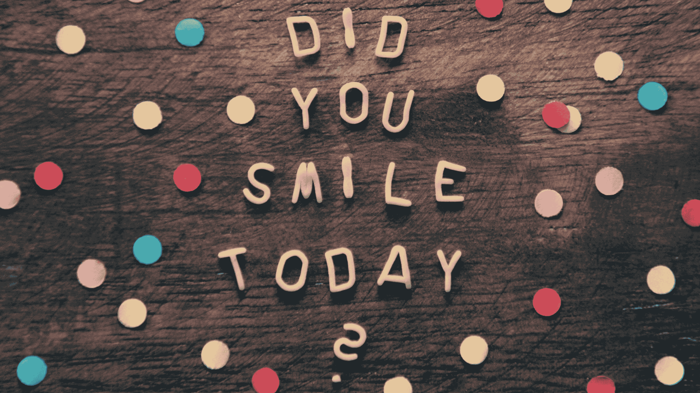 Konfetti und Buchstaben auf Holztisch formen ‚Did you smile today?‘ – persönliche Geschenke im Wandel