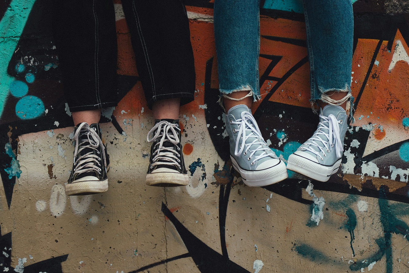 SURPRISA Blog Teenager und Geldgeschenke zwei Jugendliche sitzen auf einer Mauer man sieht nur ihre Beine und Füße blauen Jeans in schwarz-weißer Converse All Star High Top Sneakers