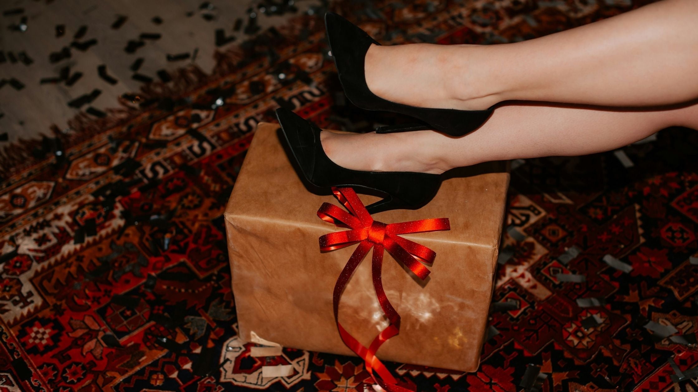 Frau legt Füße in Pumps auf Geschenk in Packpapier mit roter Schleife – entspanntes, kreatives Verpacken zu Weihnachten